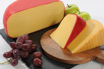 gouda and edam on wooden cutting board with grapes and apples
