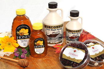 containers of honey, maple syrup and cranberries on a woode cutting board