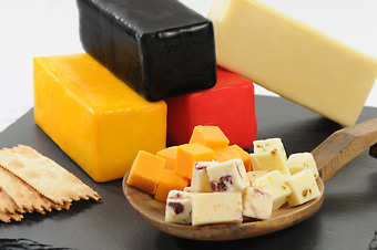 blocks of waxed cheeses on cutting board behind cubes and crackers