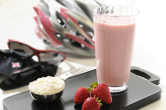 a glass of whey and strawberries in front of bike helmet and sunglasses